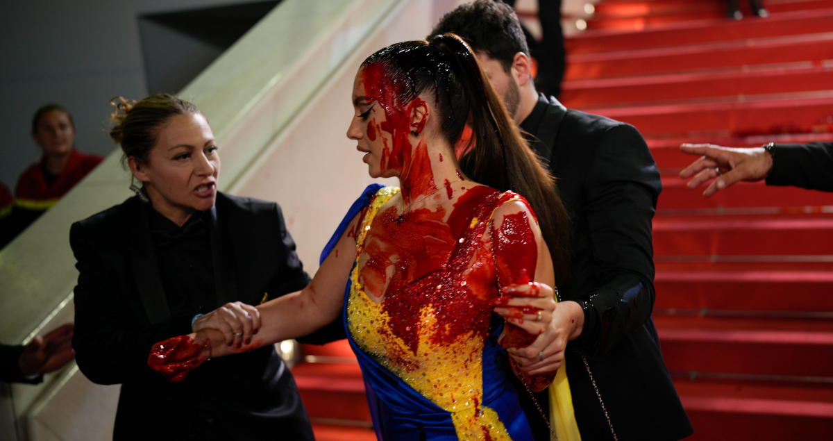 A woman dressed in blue and yellow pours fake blood on herself at the Cannes Film Festival